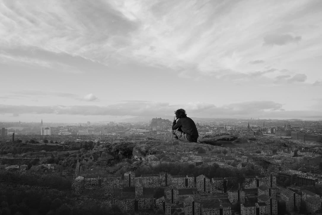 A lone figure looking out over a city skyline at dusk.